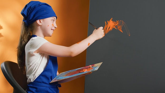 Small girl using paintbrush to create art masterpiece on canvas, holding mixing tray with wet aquarelle colors. Painting artwork with watercolor palette and brushes, artistic skills and vision.