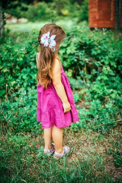 Small girl in violet pink dress in the forest