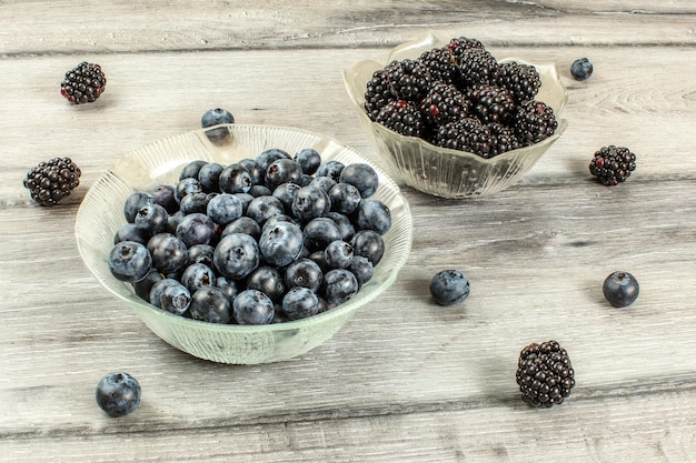 Small glass bowls with blueberries and blackberries on gray wooden desk.