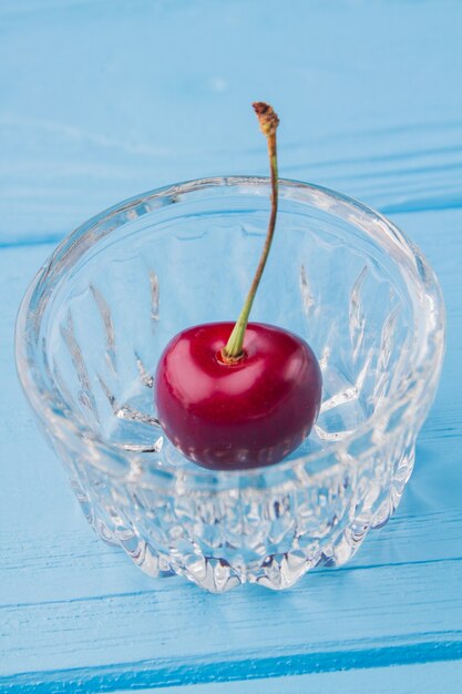 Small glass cup with one single red ripe cherry