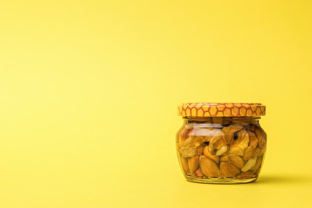 Небольшая стеклянная банка с медом и орехами на желтом фоне.