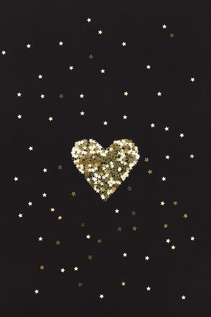 Small golden heart made of little stars on black background. christmas concept.