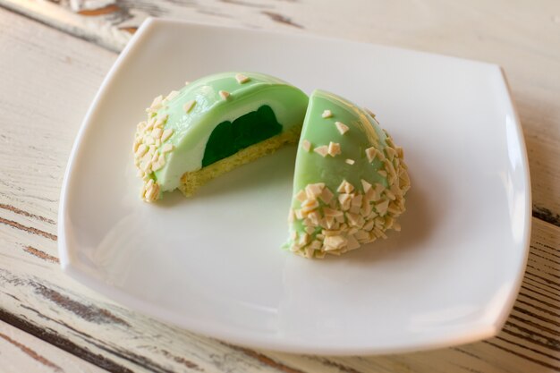 Small green cake with filling. Glazed dessert on white plate. Freshly cooked mint mousse cake. How about some sweets.