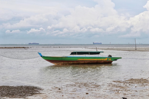 Small green river wooden motor boat for fishing and transporting tied up at the shallow sea