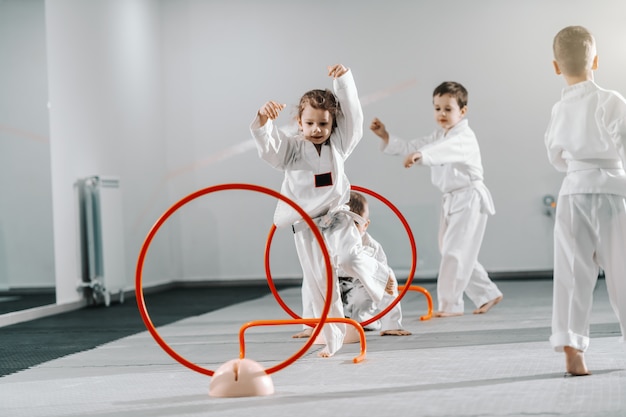 Piccolo gruppo di bambini caucasici in dobok che praticano taekwondo e si riscaldano per l'albero stando a piedi nudi.