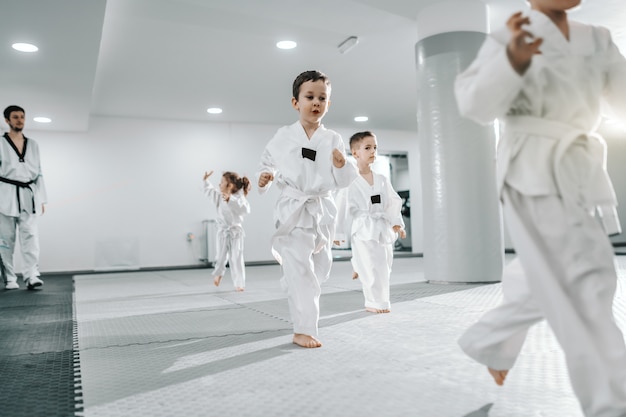 Piccolo gruppo di bambini che si allenano al corso di taekwondo. tutti vestiti di dobok. sfondo bianco.