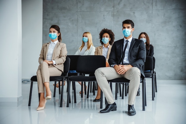 コロナウイルスのセミナーに座っているフェイスマスクを持つビジネスマンの多文化グループの小グループ