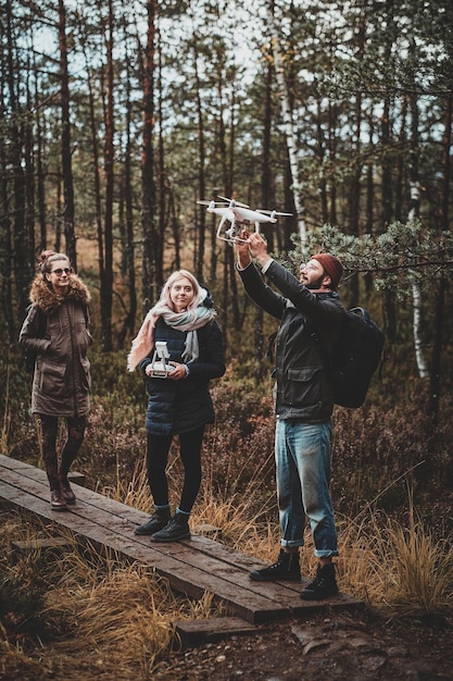 Small group of people are enjoying their hike in autumn forestal park, one of them ia making photo via drone.