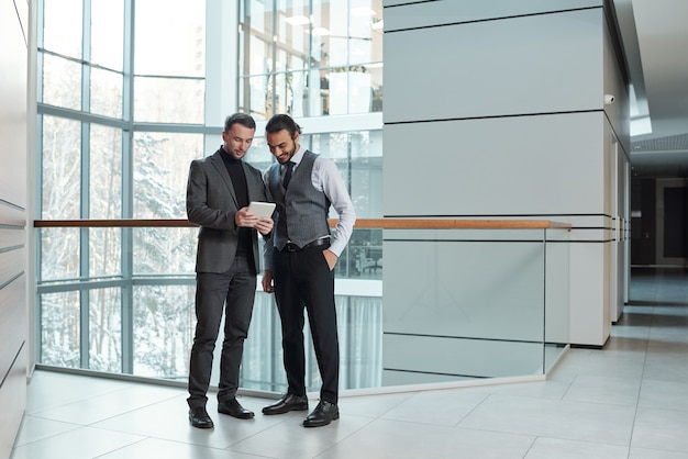 Small group of young elegant businessmen scrolling through online information while getting ready with presentation