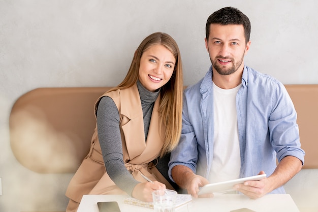 Small group of young successful employees in casualwear sitting by table in cafe at working meeting