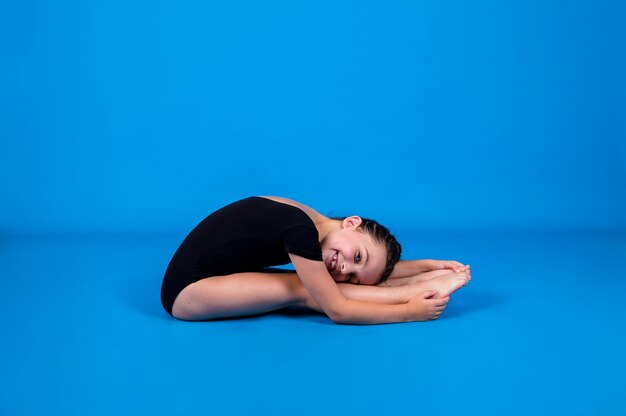 A small gymnast in a black swimsuit performs a warm-up on a blue background with a place for text