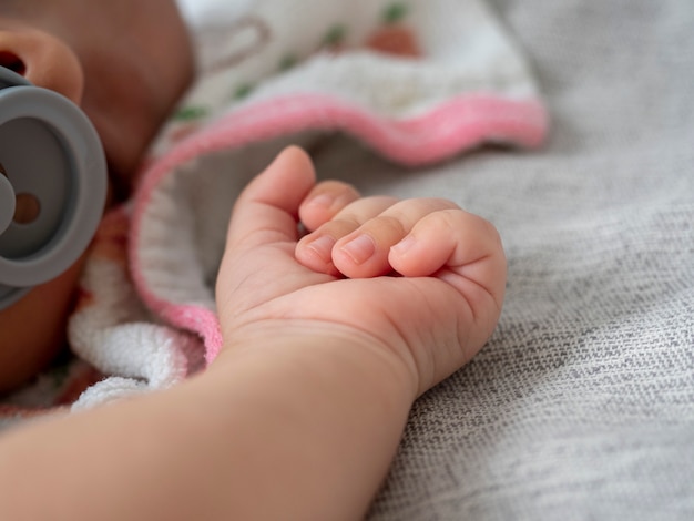 A small hand of a newborn baby lies on a gray blanket. Small children