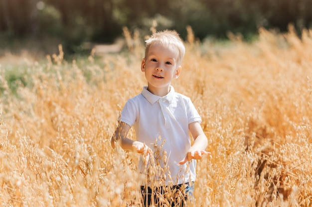A small handsome boy blonde in a white shirt in nature in the summer Happy childhood Positive emotions