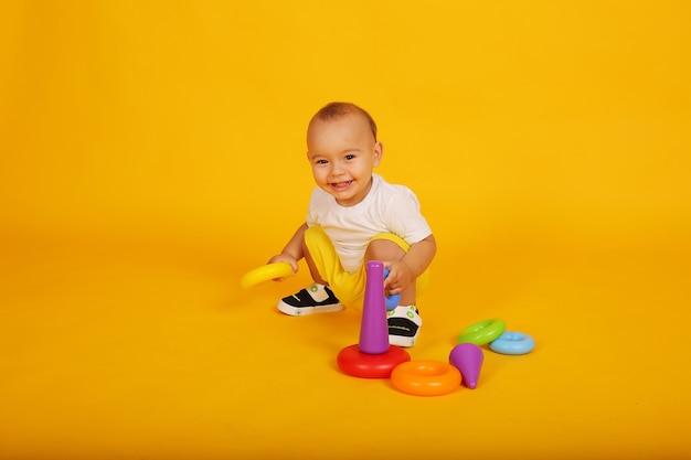 маленький счастливый мальчик в белой футболке и желтых шортах играет в игрушку-пирамиду