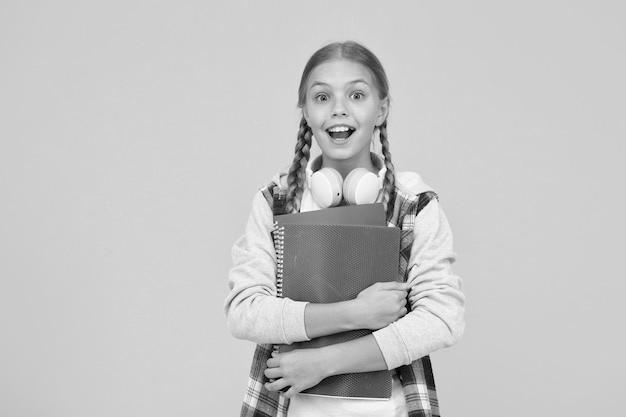 Small happy kid in earphones with notepad child ready to learn subject back to school Study lessons for exam feel the great surprise knowledge day surprised pupil yellow background copy space