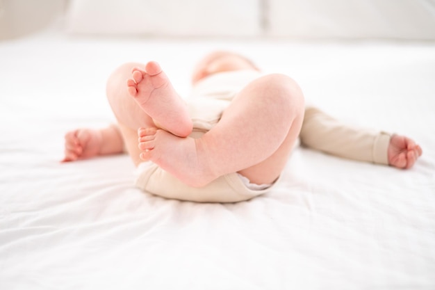 A small healthy baby in a cotton bodysuit is lying on his back on a child's bed on white bedding in the bedroom of the house the baby's legs are closeup