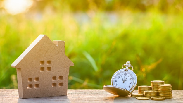 Small house model and a clock with golden coins pile