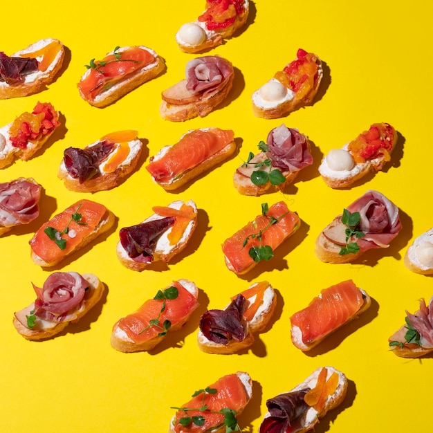 Маленькие итальянские брускетты с лососем, сливочным сыром, овощами и говядиной на желтом фоне