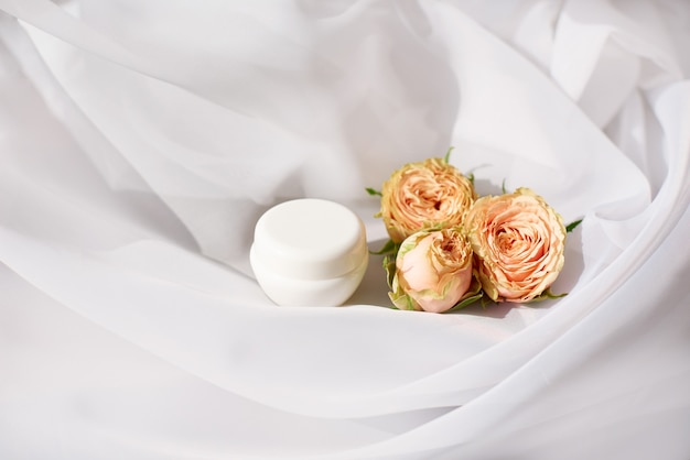 Small jar of expensive anti-aging or anti-wrinkle face cream with delicate roses on white cloth