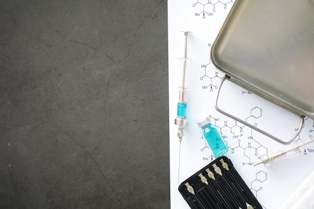 Small jars with injection and syringe for injection on blue background near the chemical formula