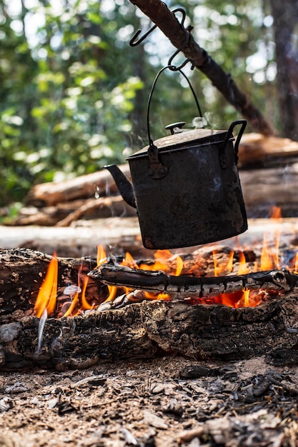 A small kettle with water is heated on a fire in a forest on a summer sunny day Closeup