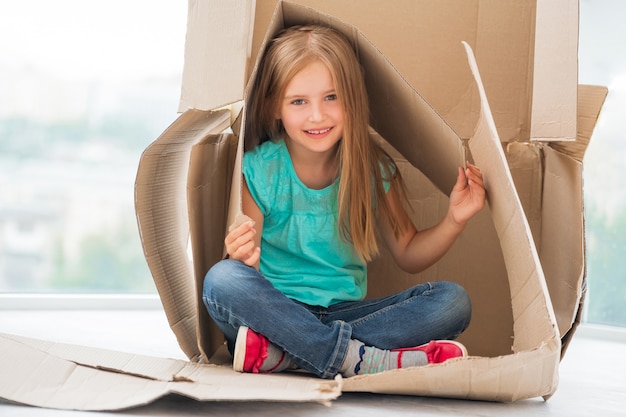 Small kid girl sitting in cardboard house