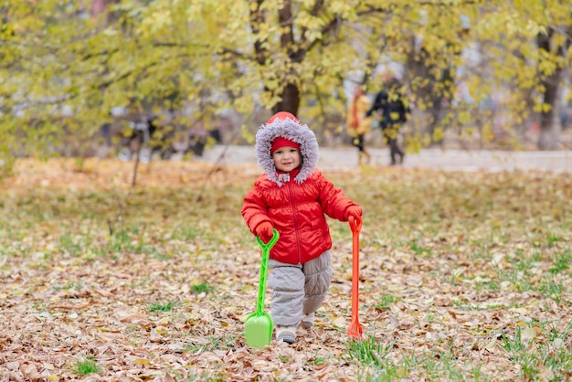 A small kid with a rake and a shovel walks in the park