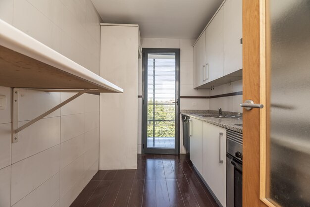 small kitchen furnished with white furniture and gray granite countertop wooden and glass access door to the kitchen and access to a terrace with glass and gray aluminum door