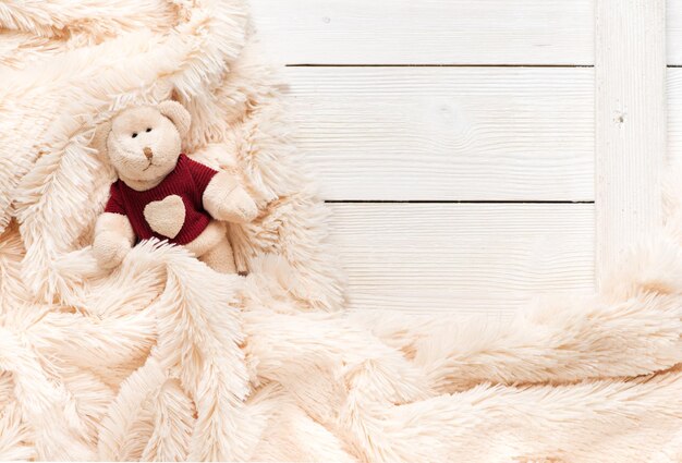 Маленький вязаный медвежонок накрыт теплым одеялом, вид сверху