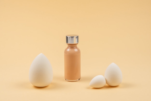 Small, medium and large  white beauty blender and makeup foundation on beige background.