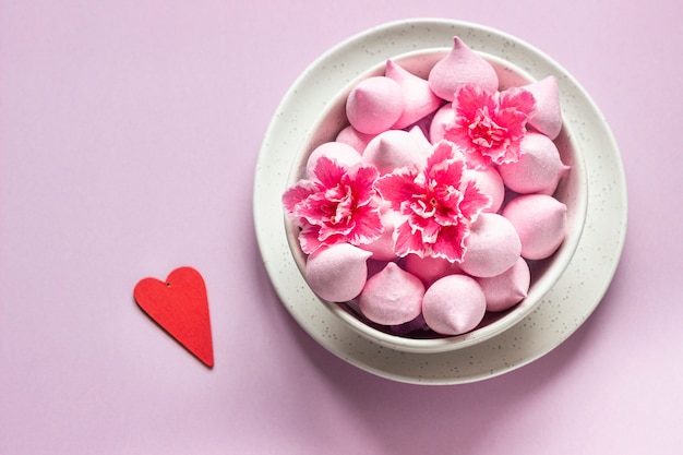 Small meringues and pink flowers in a ceramic bowl. Gift for Valentine's Day.