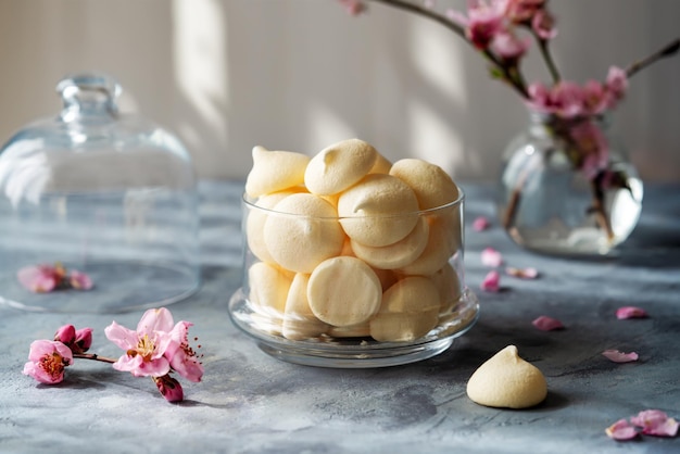 Small meringues in a white bowl over light pink background decorated with spring flowers