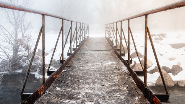 Foto un piccolo ponte di metallo su un ruscello che lascia nella nebbia.