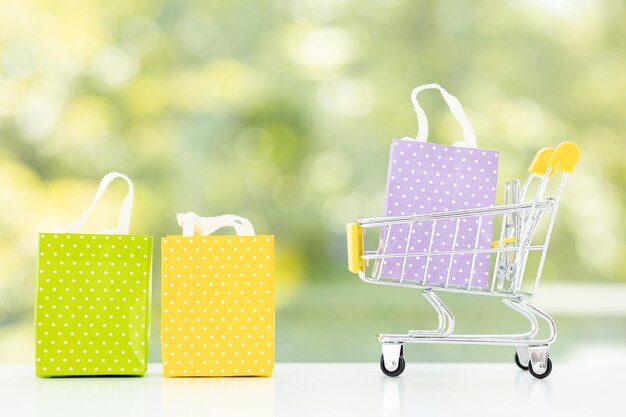 Small metal cart with shopping bags on green summer background