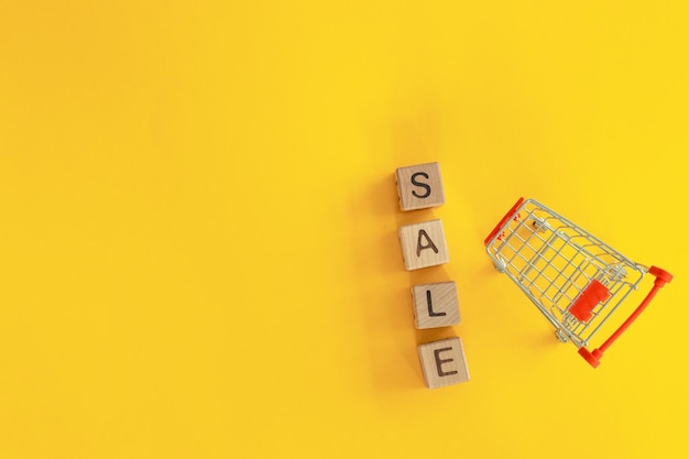 Small metal cart and word sale on yellow background Shopping concept