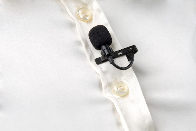 Маленький микрофон на прищепке для записи голоса прикреплен к женской рубашке на груди