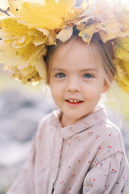 Small mysteriously smiling girl in a wreath of yellow leaves portrait