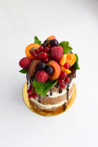 Small naked round cake decorated with berries on a white background