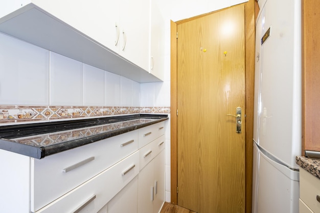 Photo small narrow kitchen with countertop over lots of white drawers with metal handles and black oak wood door