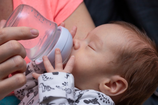 Il piccolo neonato beve il latte da una bottiglia