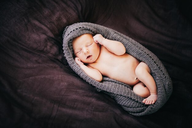 A small newborn child lies on a brown plaid