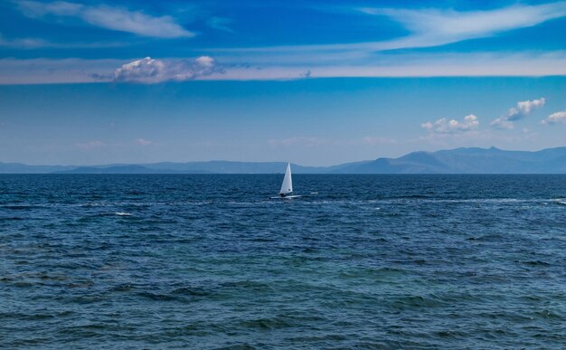 Small optimist boat with white sail blue sky and sea background