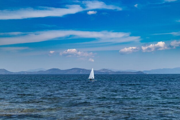 白い帆の青い空と海の背景を持つ小さな楽観的なボート