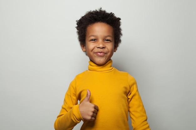 Small optimistic black child boy smiling and showing thumb up on white background