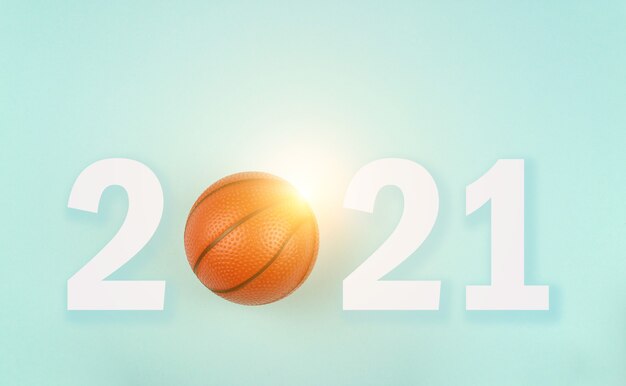 Small orange ball for basketball sport game on blue background with text 2021 and sunshine.