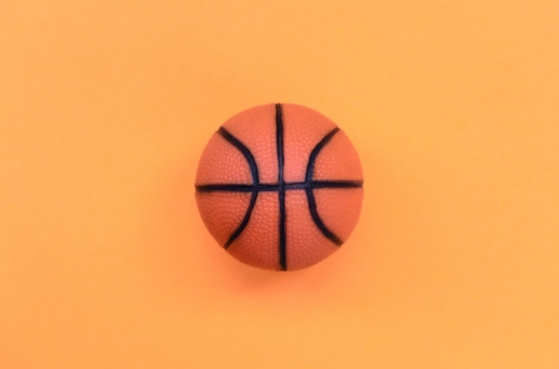 Маленький оранжевый шарик для спортивной баскетбольной игры лежит на текстурном фоне из бумаги пастельного оранжевого цвета в минимальной концепции