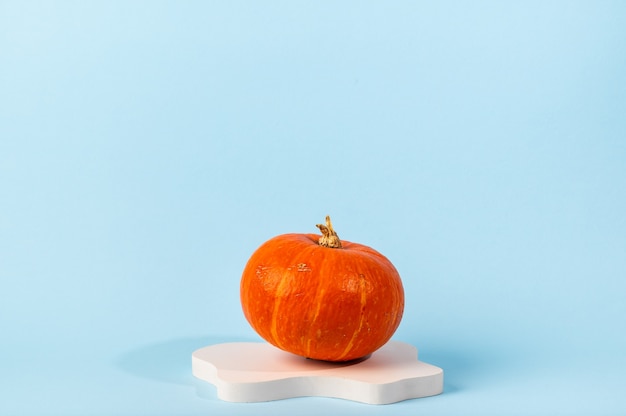 Small orange pumpkin on blue background with copy space. Concept celebration of Halloween or Thanksgiving. Cosmetics podium for halloween. Autumn still life.