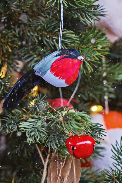 Small ornamental bullfinch hanging on Christmas tree branch