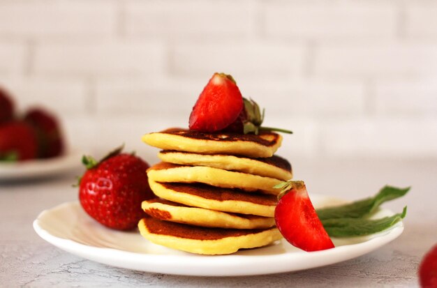 Small pancakes stacked on a plate with strawberries on a light background