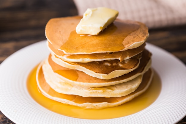 Small pancakes with maple syrup and butter on wooden table